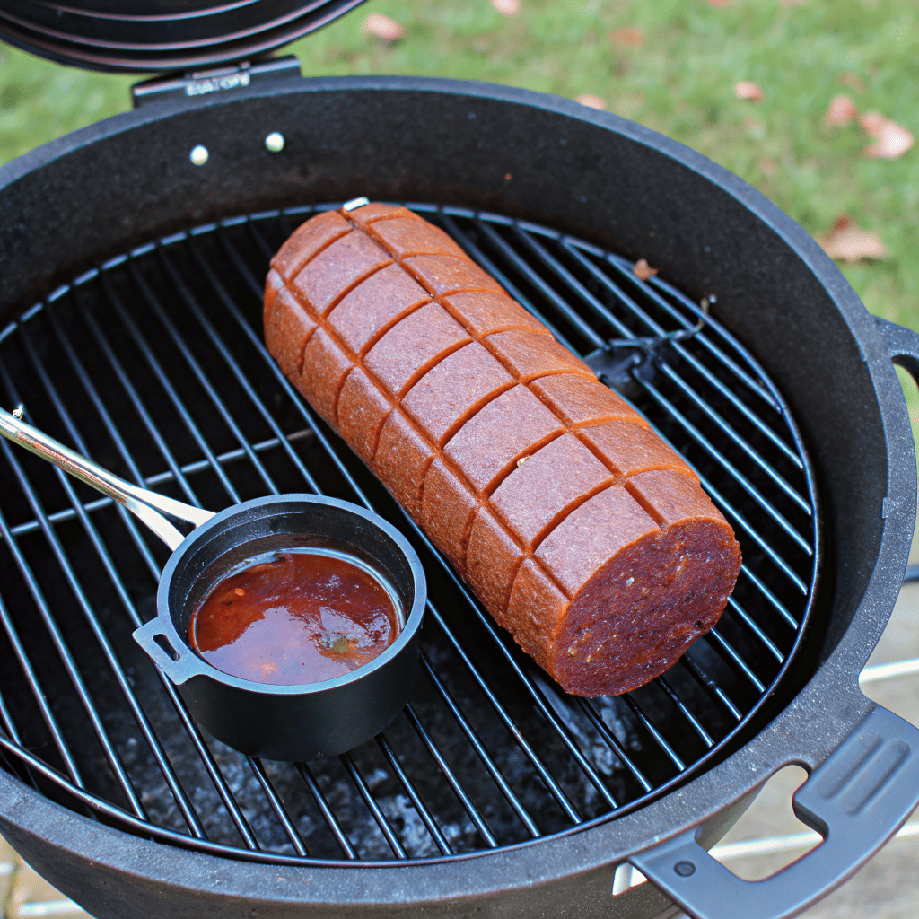 smoked bologna scored with glaze simmering on smoker